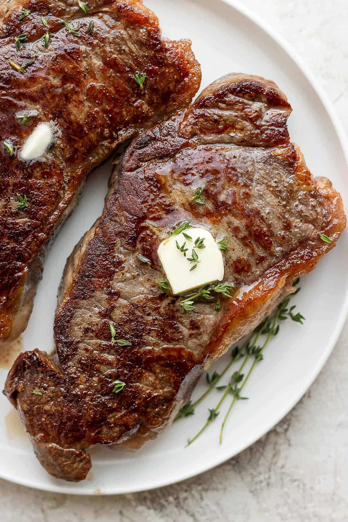 Sous vide steaks on a plate with butter and some fresh thyme on top.