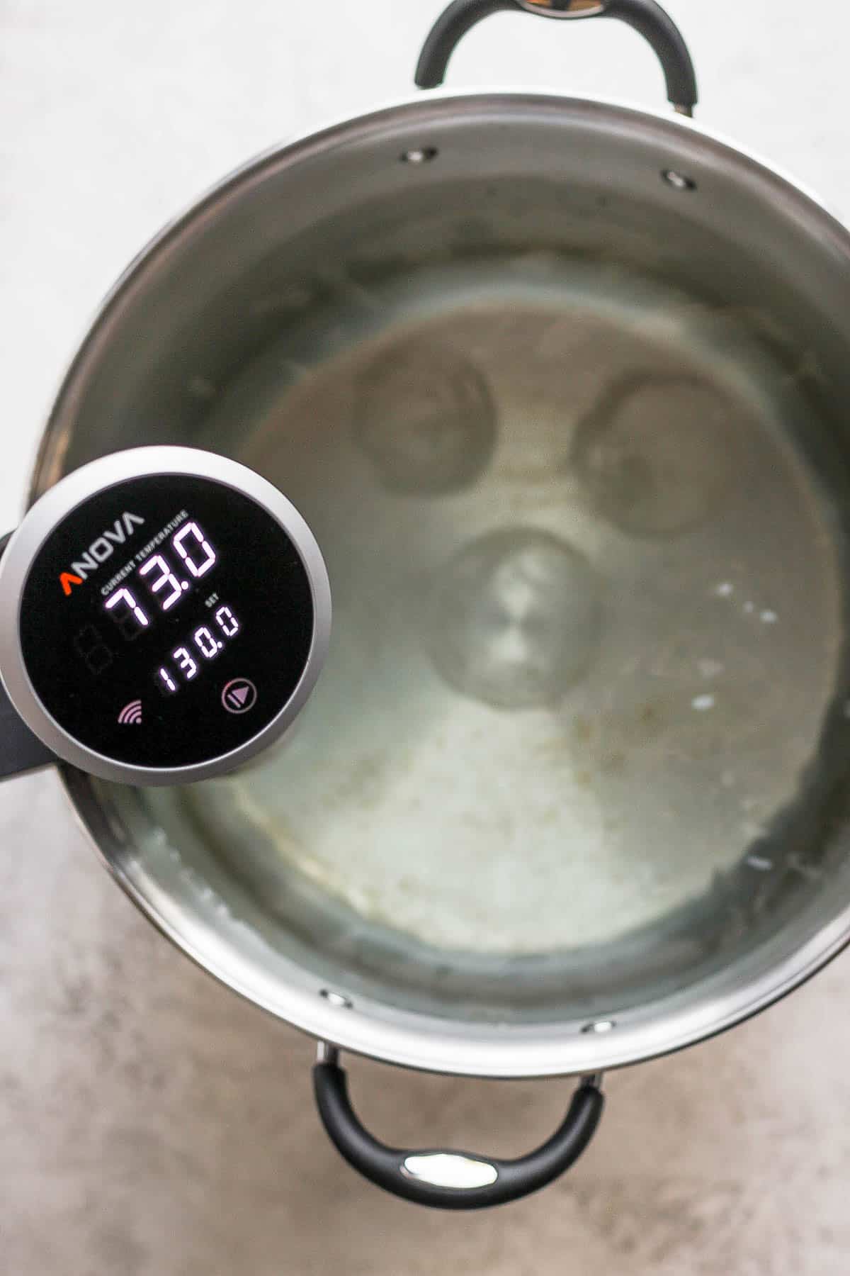 A sous vide set to 130 degrees attached to the side of a pot of water.