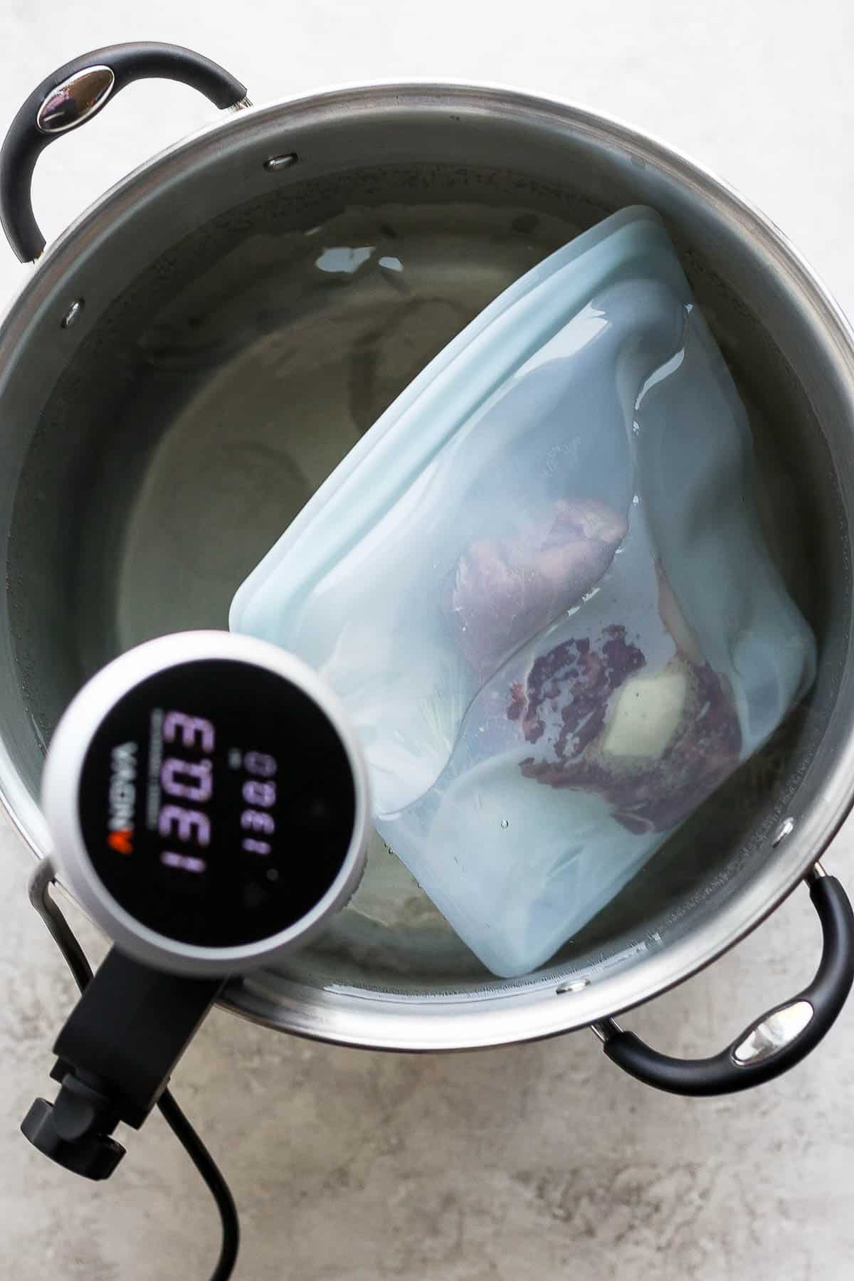 Plastic bag with steak submerged in the pot of water.