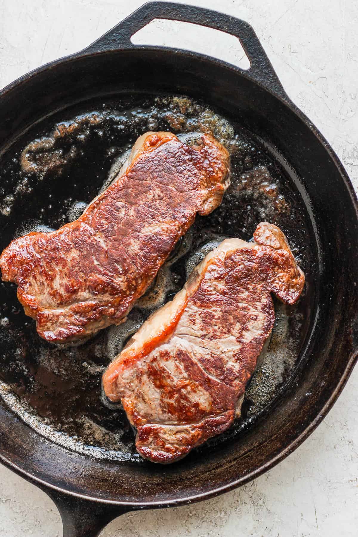 Steaks searing in a cast iron skillet.