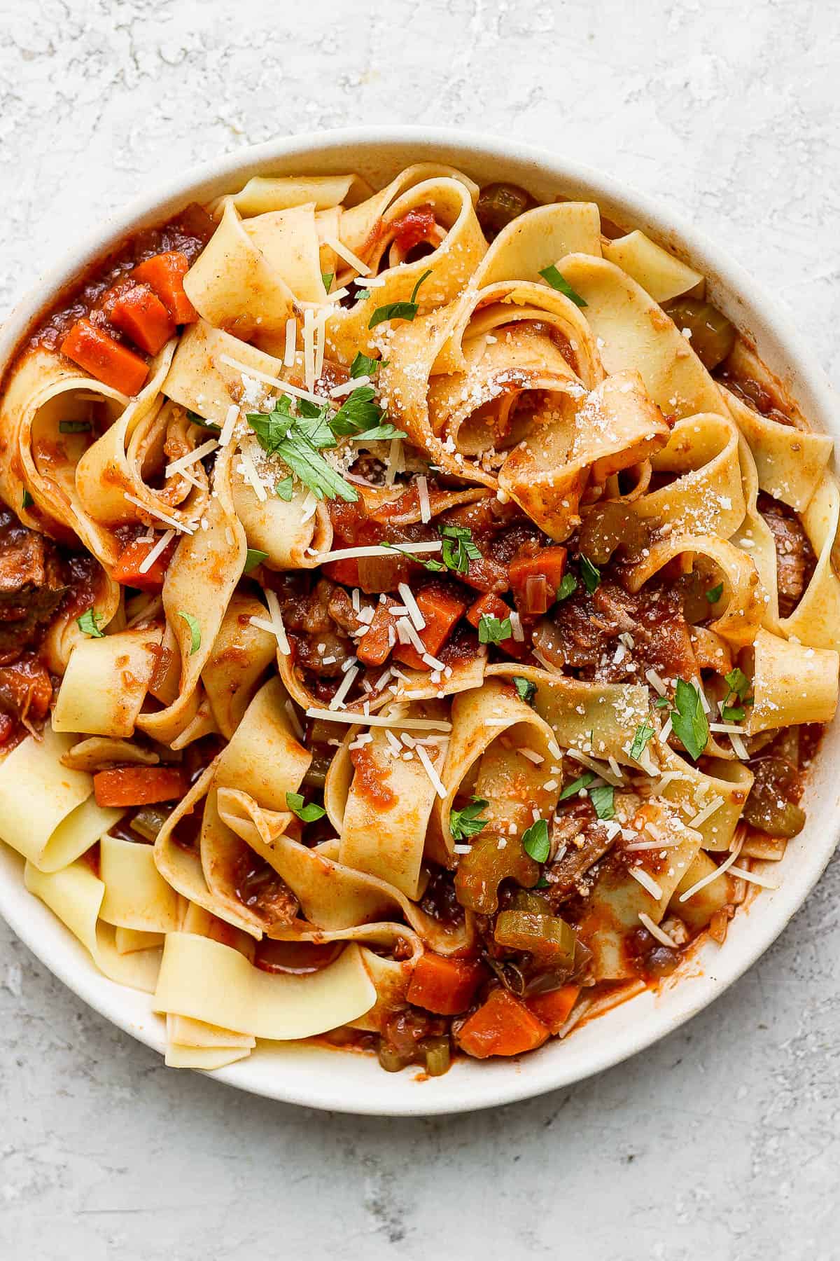 Lamb ragu with pappardelle pasta in a white bowl. 