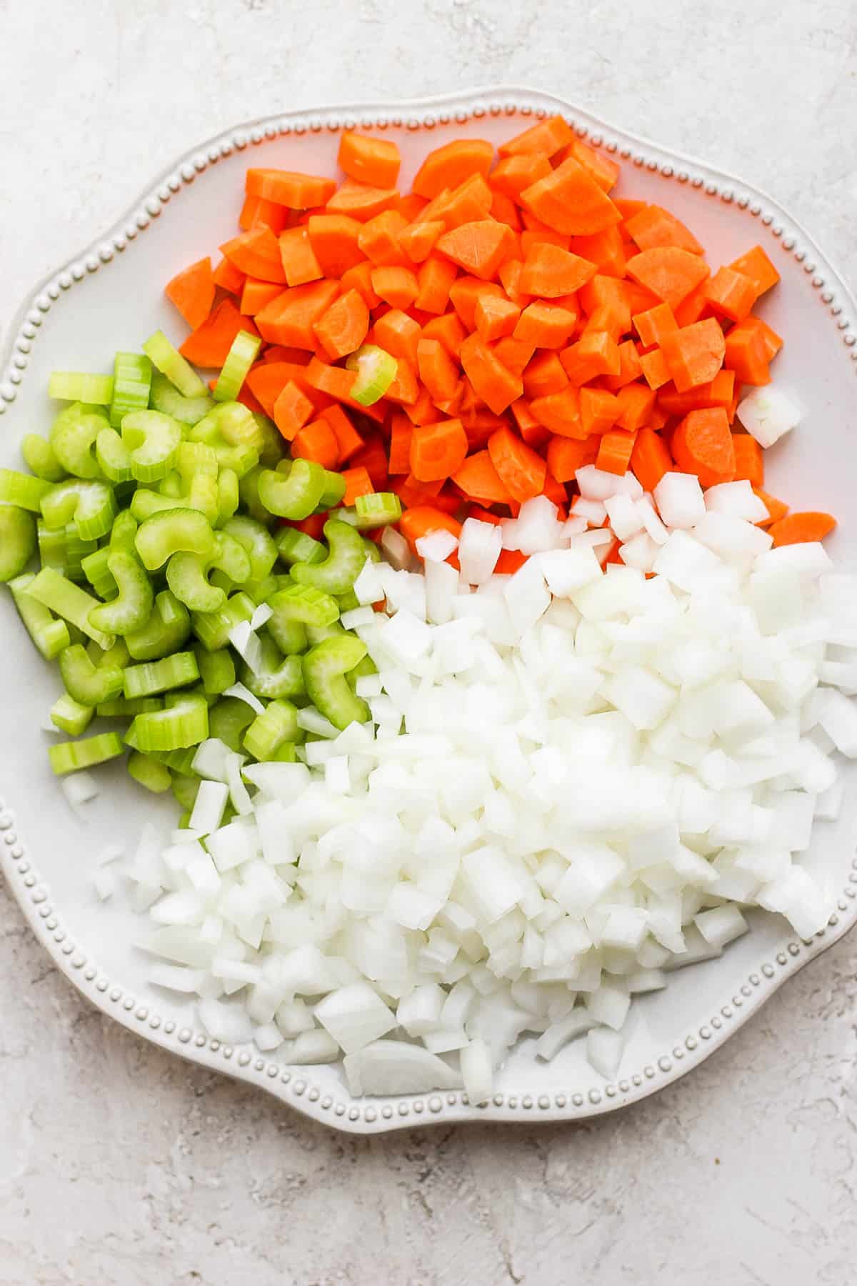 Diced onion, chopped carrots, and chopped celery on a white plate.