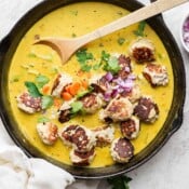 Cast iron skillet filled with meatball curry with wooden spoon sticking out.