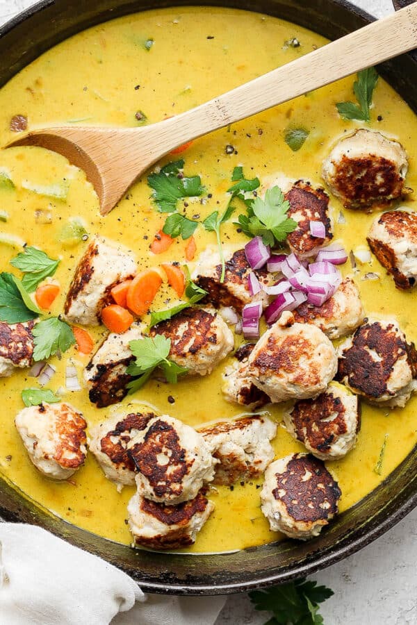 Cast iron skillet filled with meatball curry with wooden spoon sticking out.