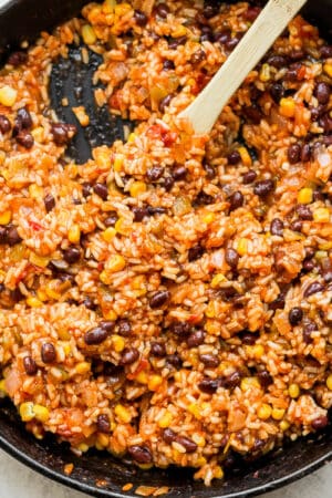Cast iron skillet filled with salsa rice with wooden spoon sticking out.