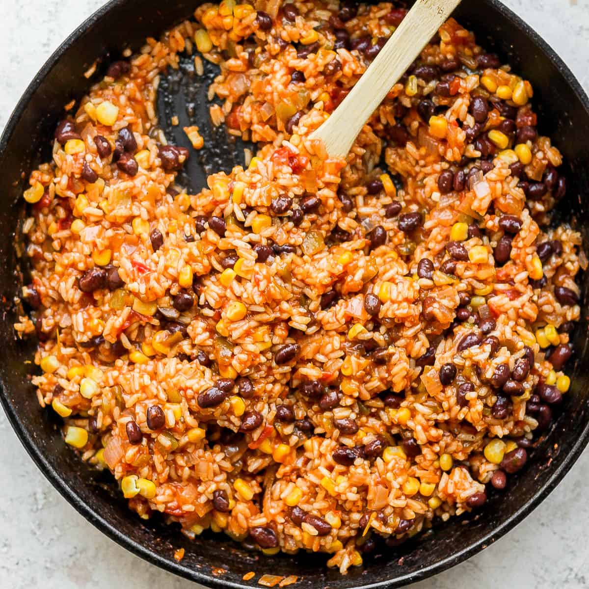 Cast iron skillet filled with salsa rice with wooden spoon sticking out.