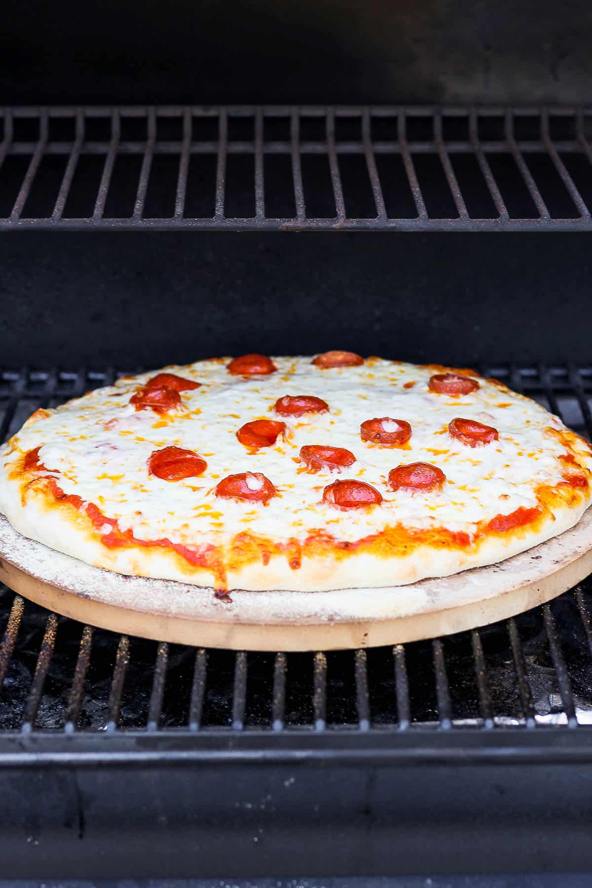 A pizza cooking on a pizza stone sitting on the grill grates on a smoker. 