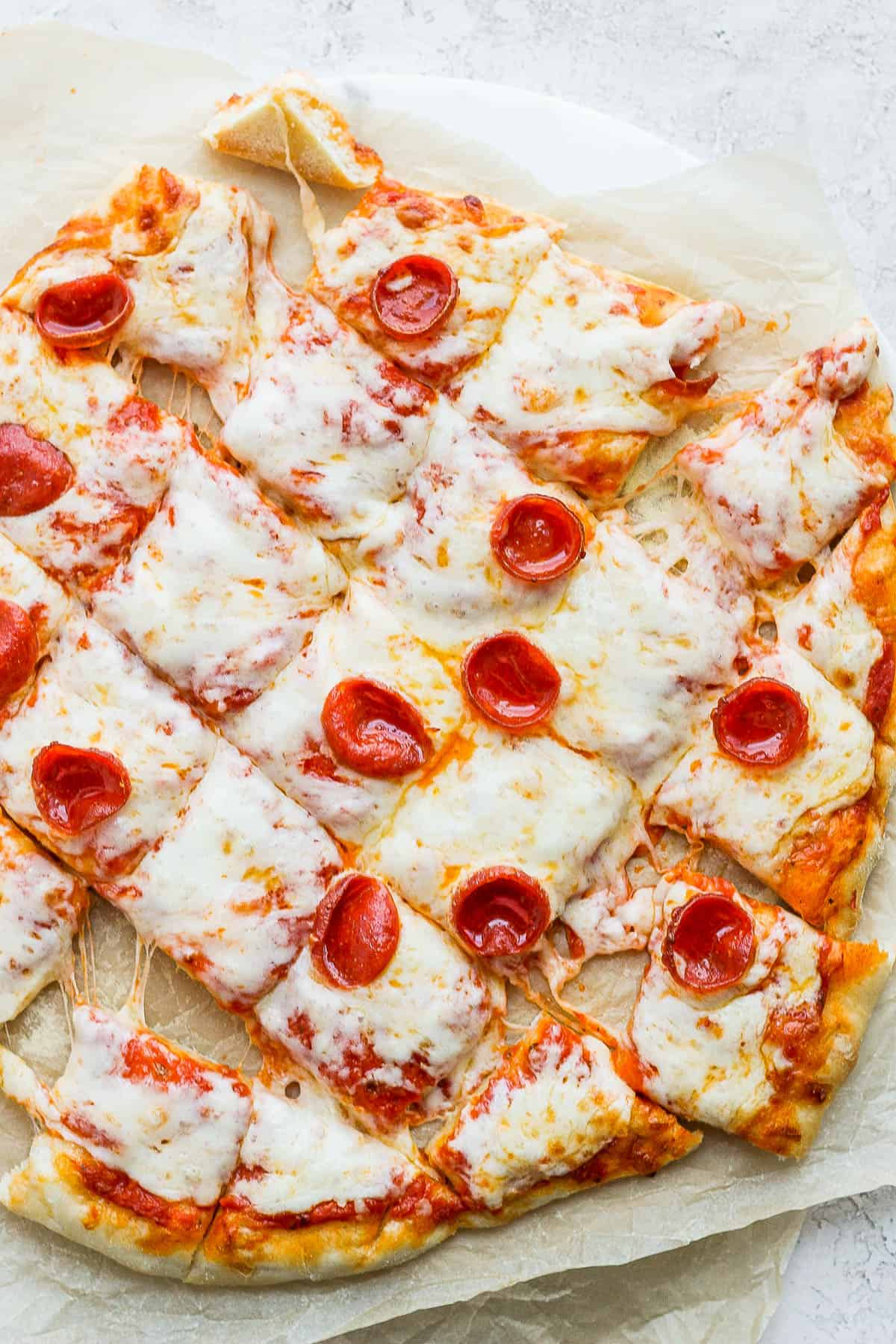 A smoked pizza on some parchment paper cut into squares.