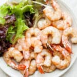 Plate of smoked shrimp with salad greens next to them.