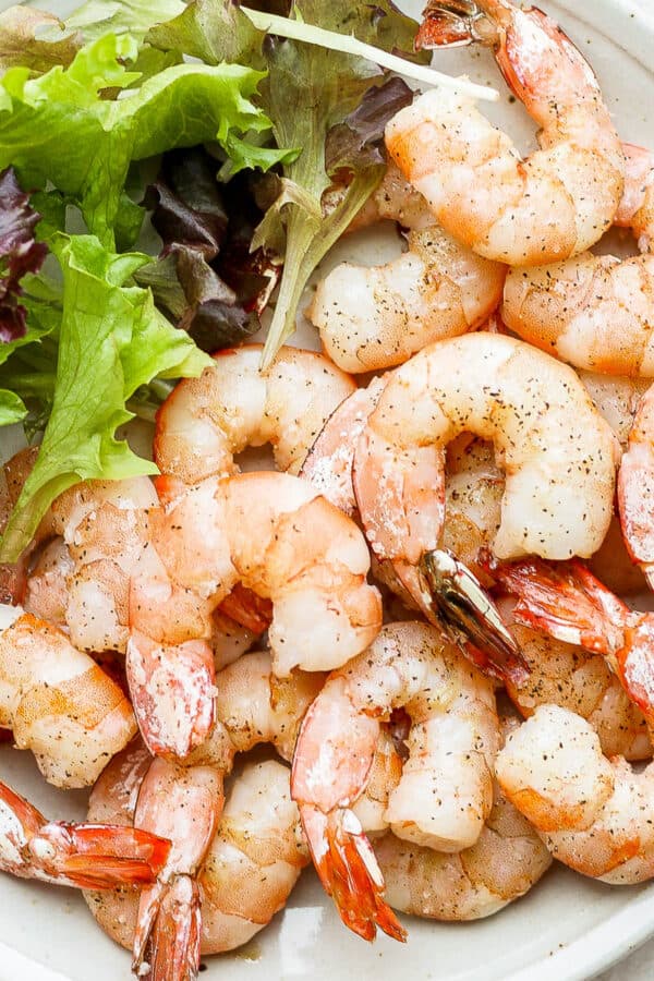 Plate of smoked shrimp with salad greens next to them.