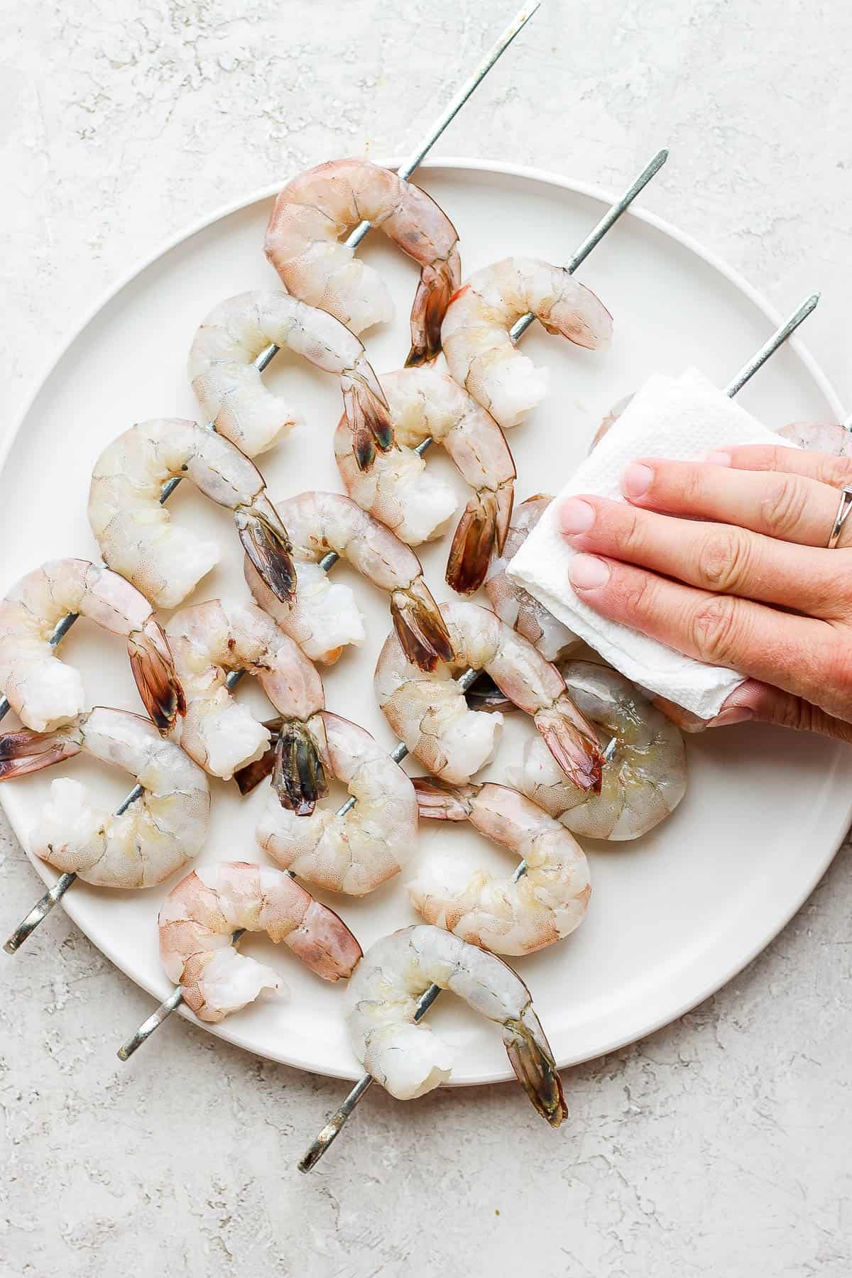 Raw shrimp on skewers and being pat dry.