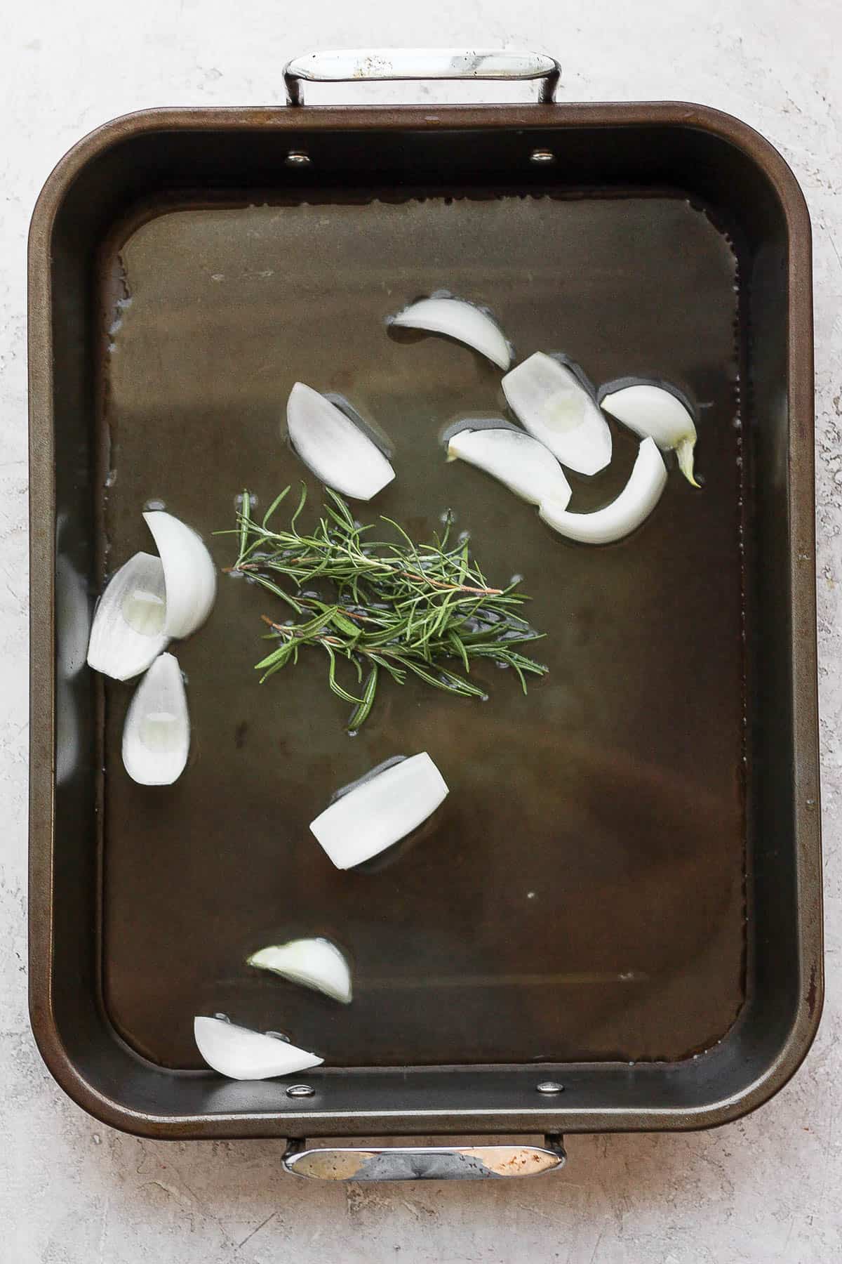 A roasting pan with chicken broth, onion, and herbs.