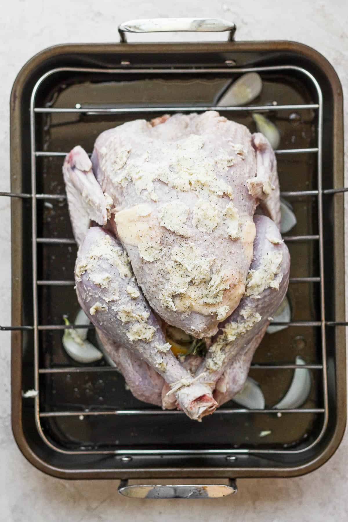 The turkey placed on the roasting rack and it has been covered in herbed butter.