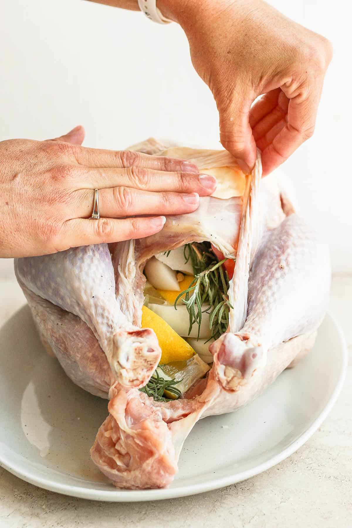 An orange, onion, and fresh herbs stuffed in the turkey and butter being placed under the skin.