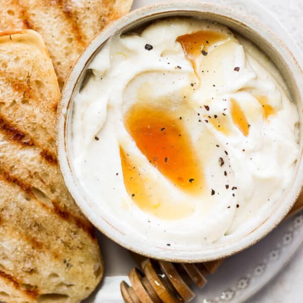 Whipped ricotta in a bowl with honey and pepper on top next to a few pieces of grilled bread.