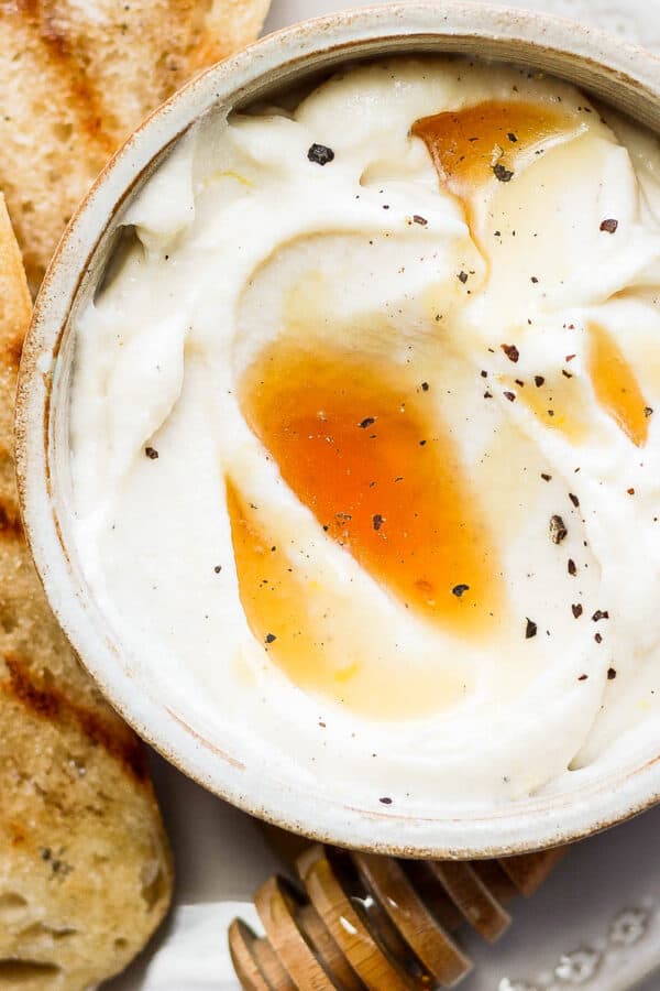 Whipped ricotta in a bowl with honey and pepper on top next to a few pieces of grilled bread.