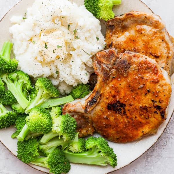 A plate with two baked pork chops, mashed potatoes and broccoli.