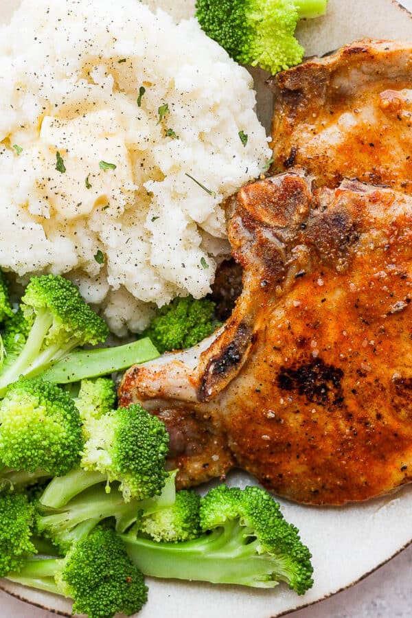 A plate with two baked pork chops, mashed potatoes and broccoli.