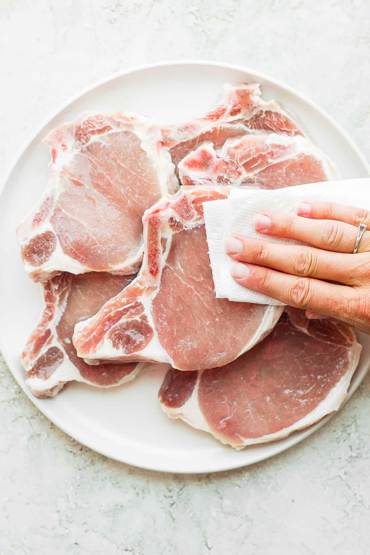 Pork chops on a plate being patted down with a clean paper towel. 
