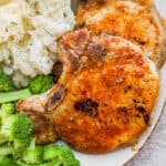 Close up of two baked pork chops on a plate with mashed potatoes and broccoli.