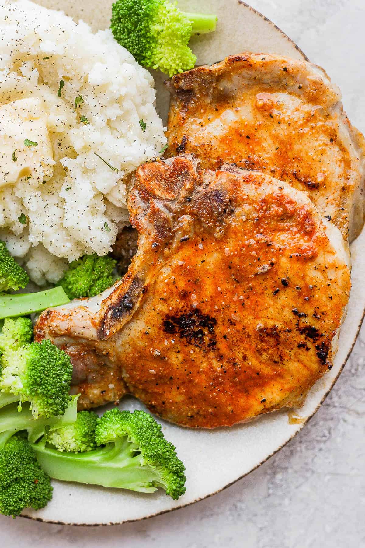 Baked pork chops on a plate with side dishes of mashed potatoes and broccoli. 