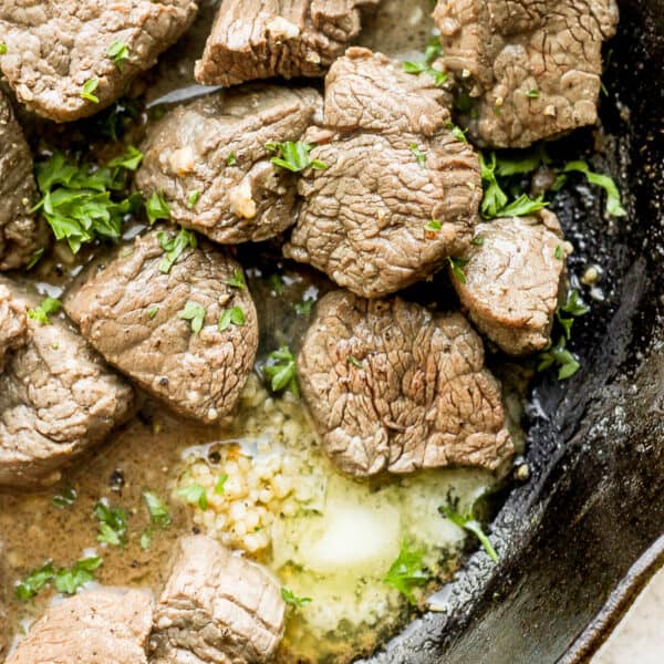 Cast iron skillet filled with beef tenderloin steak tips with butter, garlic and herbs.
