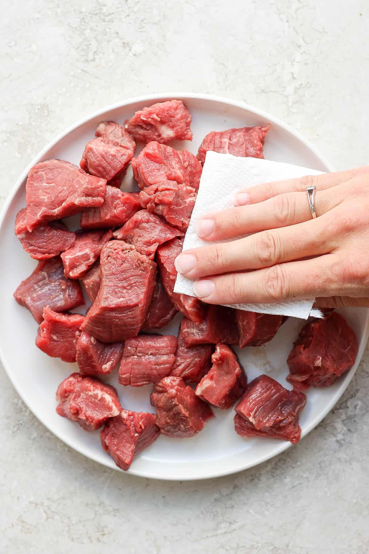 Steak tips being pat dry with paper towel.