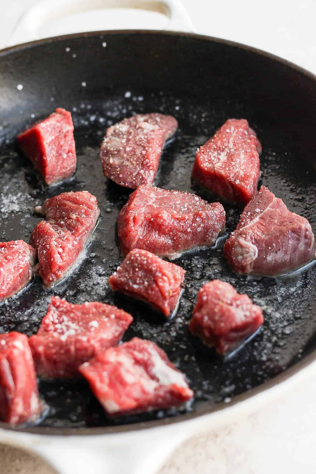 Beef tenderloin steak tips searing in a cast iron skillet.