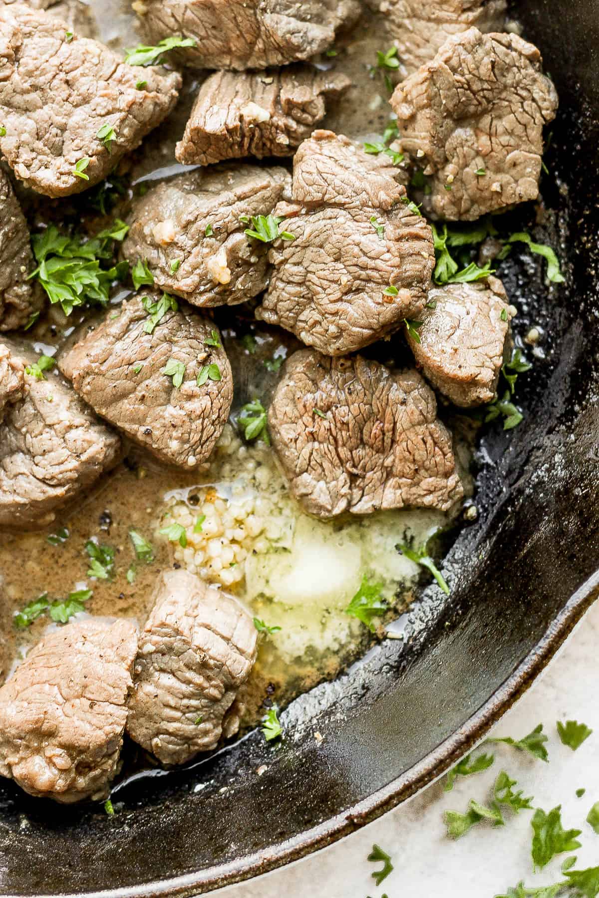 Beef tenderloin steak tips in the skillet with butter, garlic, and fresh parsley.