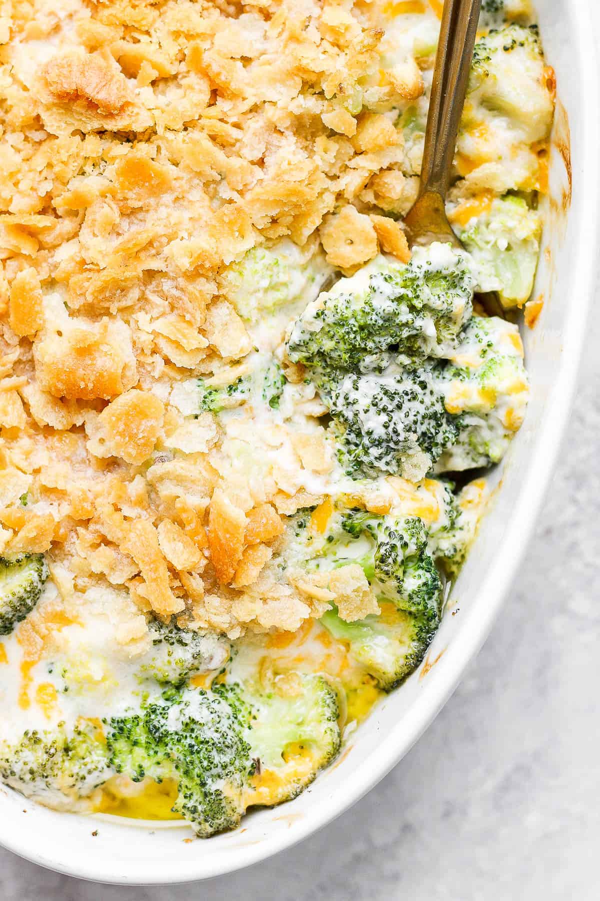 A close up image of the baked broccoli casserole with a spoon pulling out a small section to show a piece of broccoli coated in the cream mixture. 