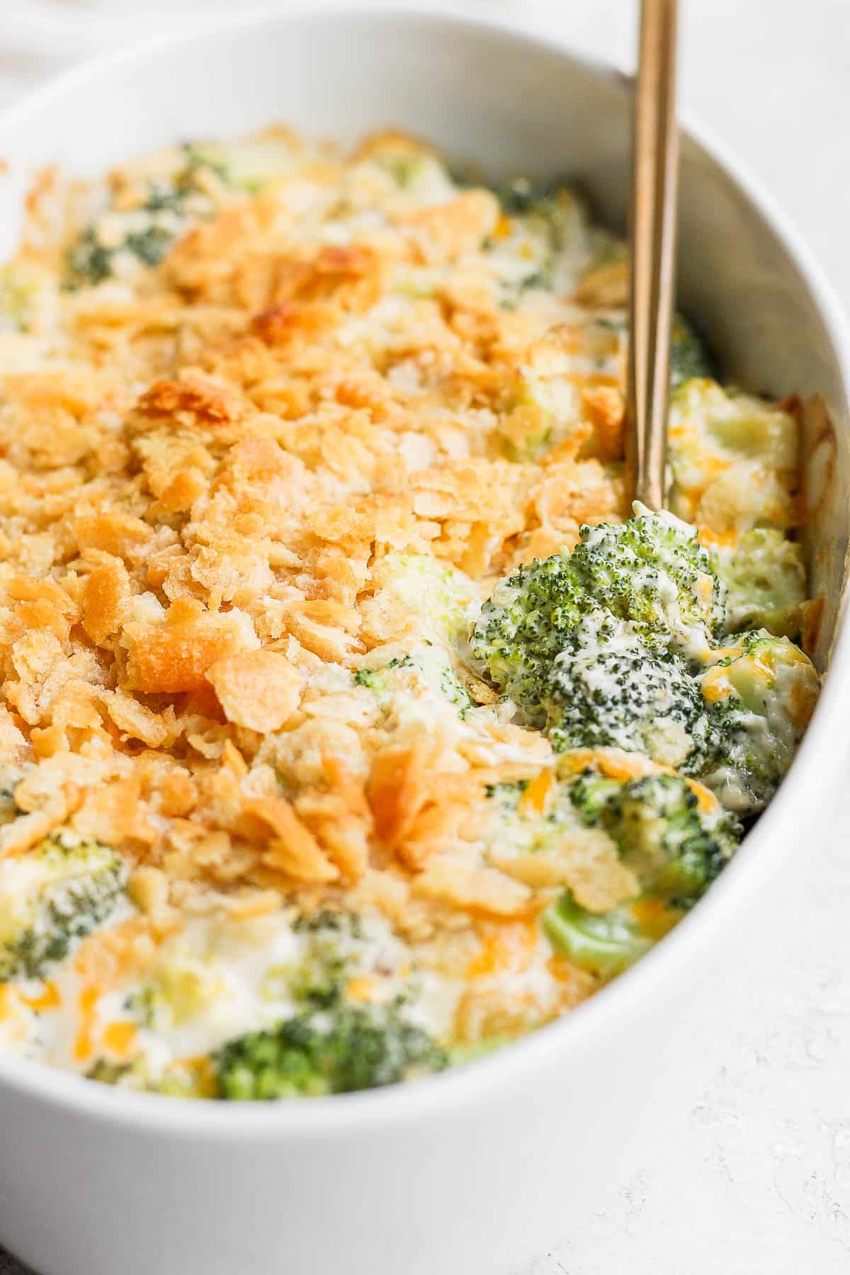 A close up image of the baked broccoli casserole with a spoon pulling out a small section to show a piece of broccoli coated in the cream mixture. 