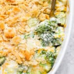 A casserole pan filled with broccoli casserole with a spoon sticking out of it.