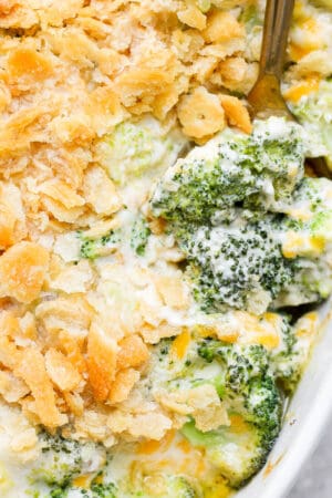 A casserole pan filled with broccoli casserole with a spoon sticking out of it.
