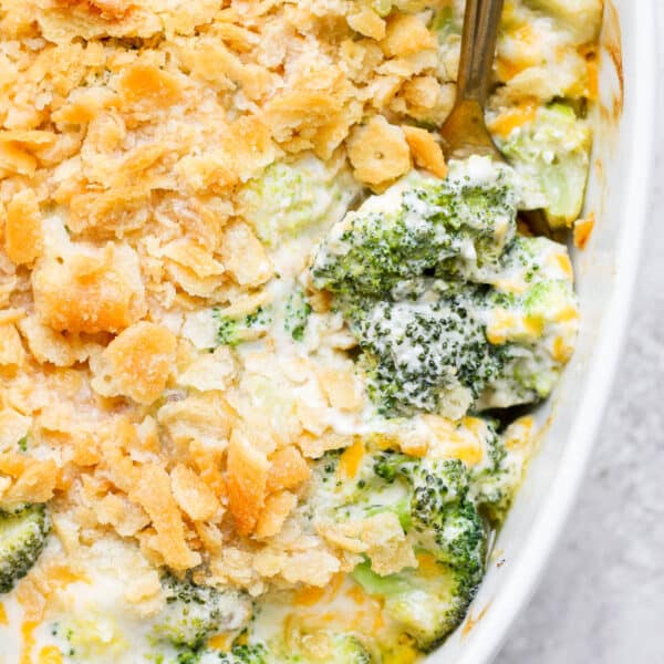 A casserole pan filled with broccoli casserole with a spoon sticking out of it.