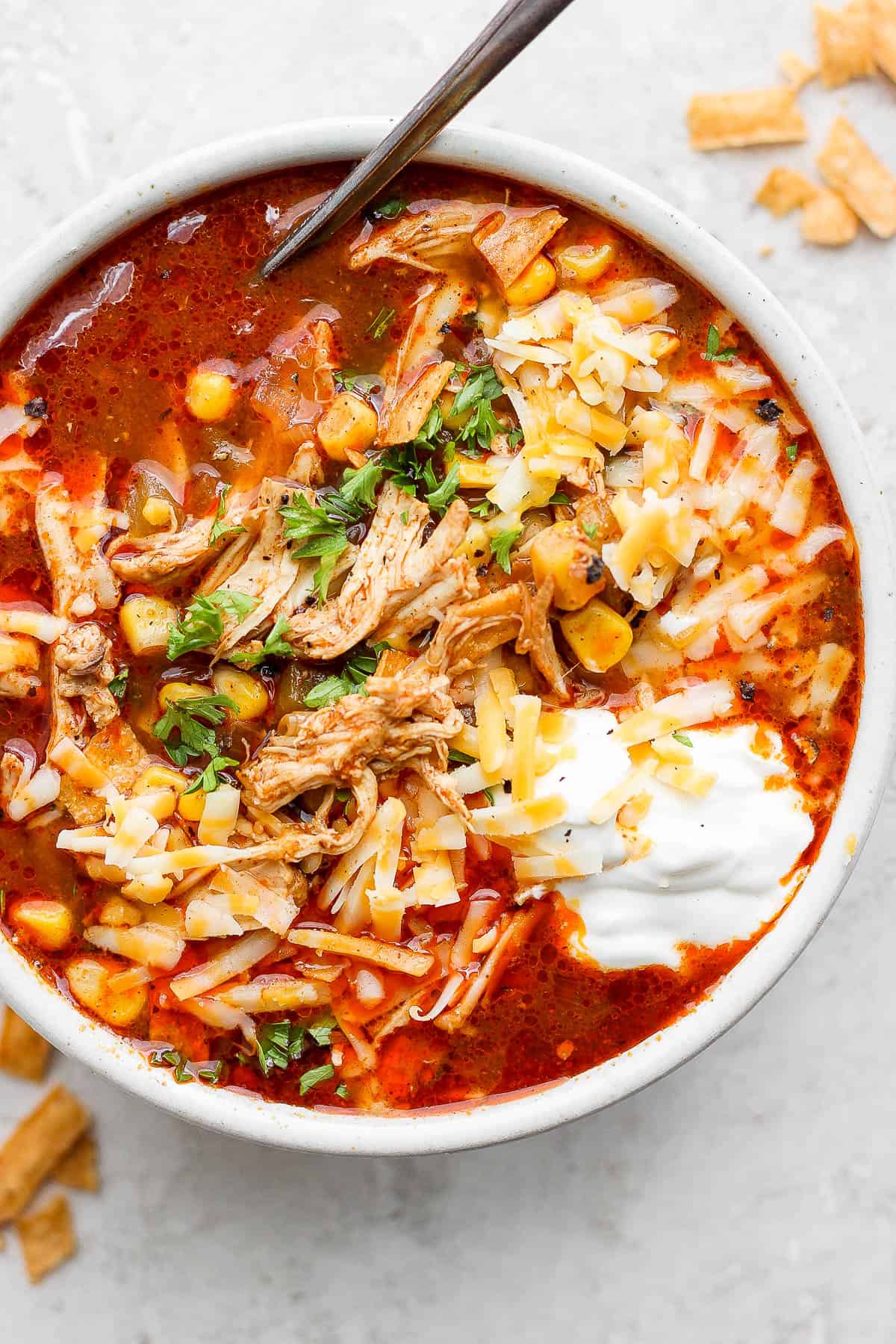 A finished bowl of chicken enchilada soup topped with sour cream, cilantro, and shredded cheese.