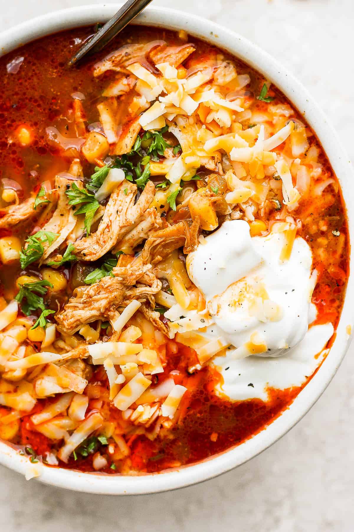 A close up shot of chicken enchilada soup in a bowl topped with cilantro, sour cream, and shredded cheese. 