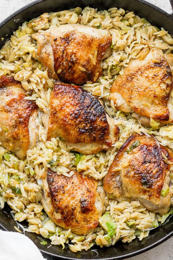 A cast iron skillet filled with parmesan orzo and chicken thighs.