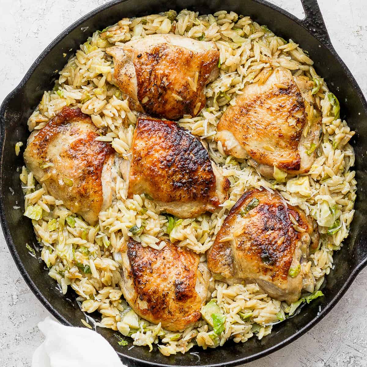 A cast iron skillet filled with parmesan orzo and chicken thighs.