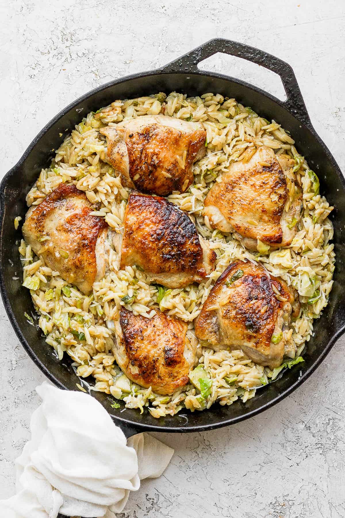 Fully cooked orzo in the skillet with the chicken thighs.