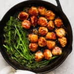 Cast iron skillet filled with teriyaki chicken meatballs and broccolini.