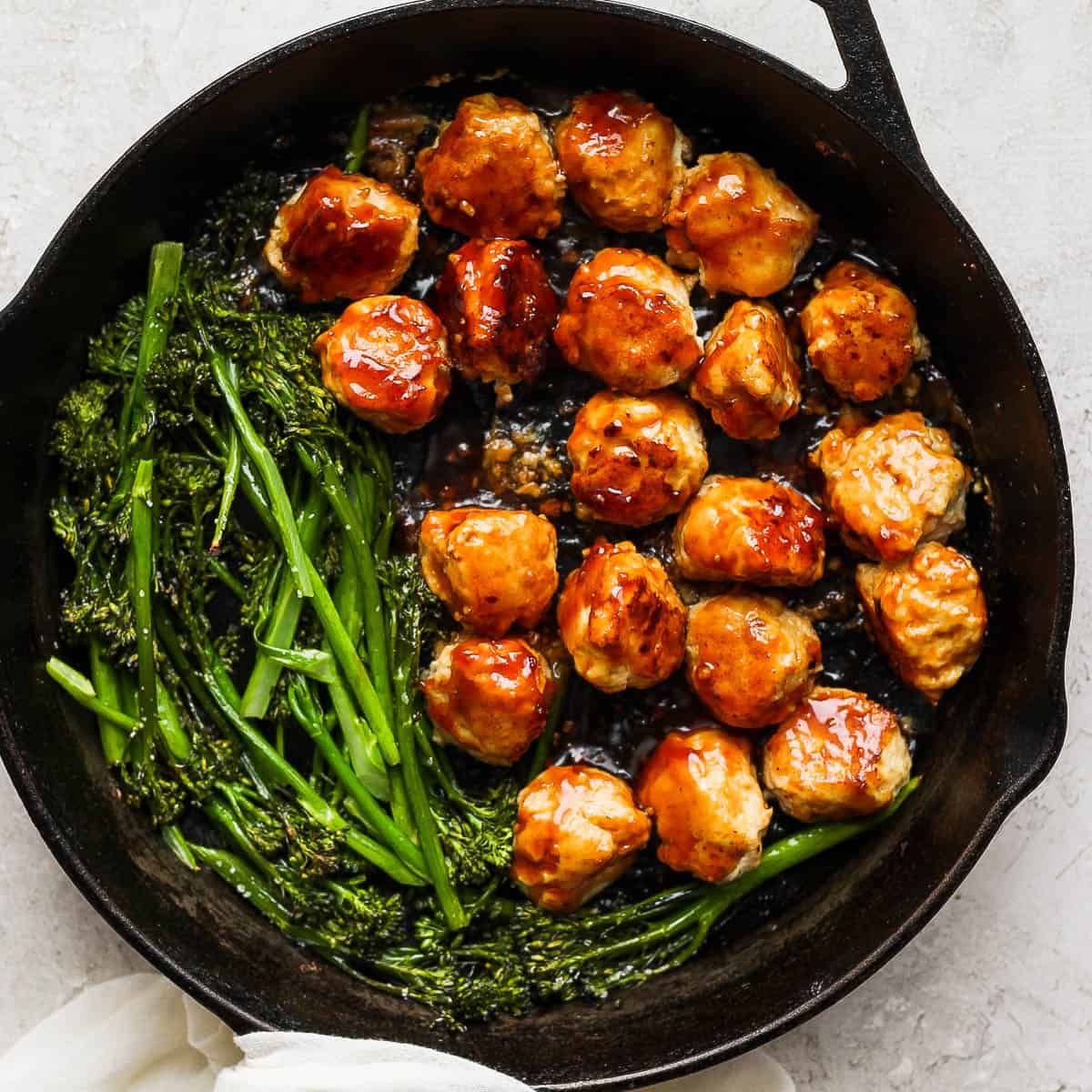 Cast iron skillet filled with teriyaki chicken meatballs and broccolini.