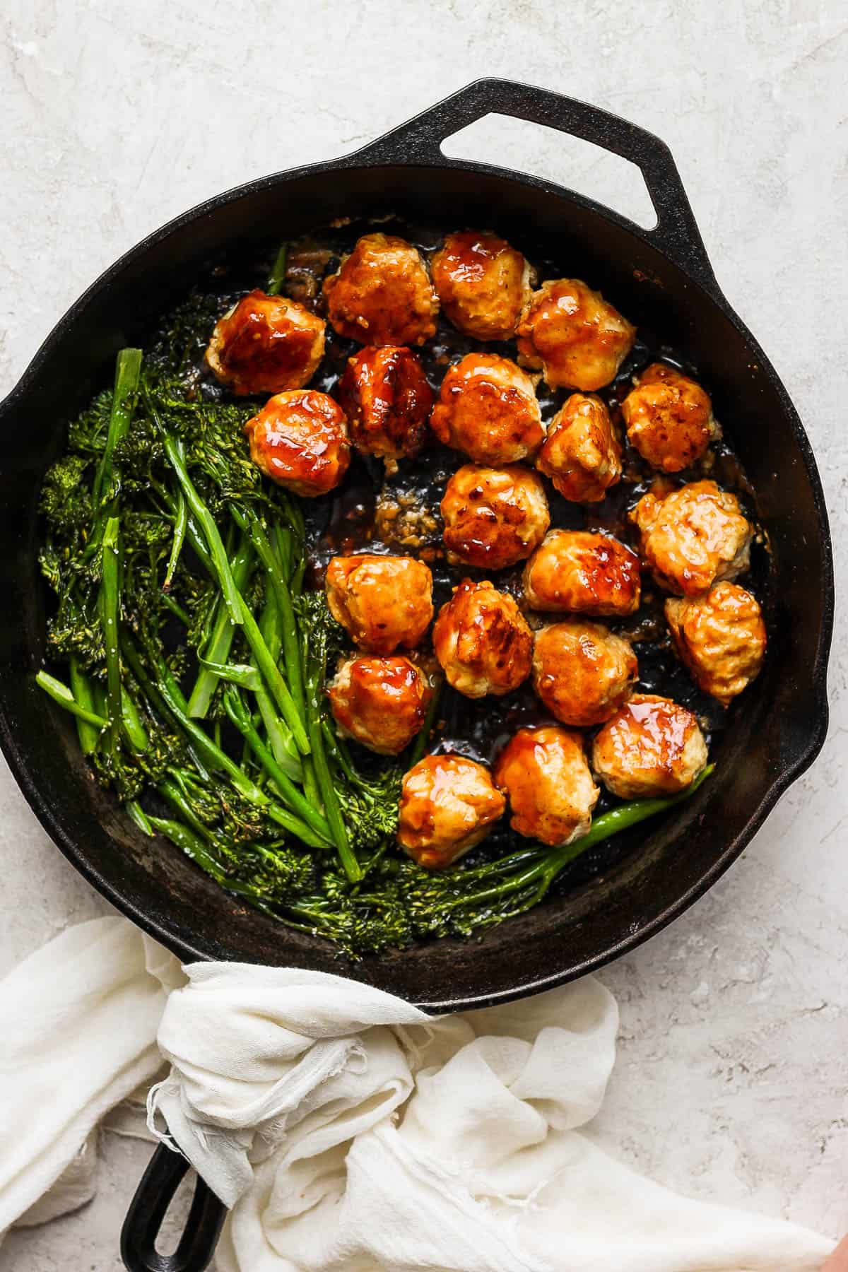Chicken teriyaki meatballs in a skillet with broccolini.