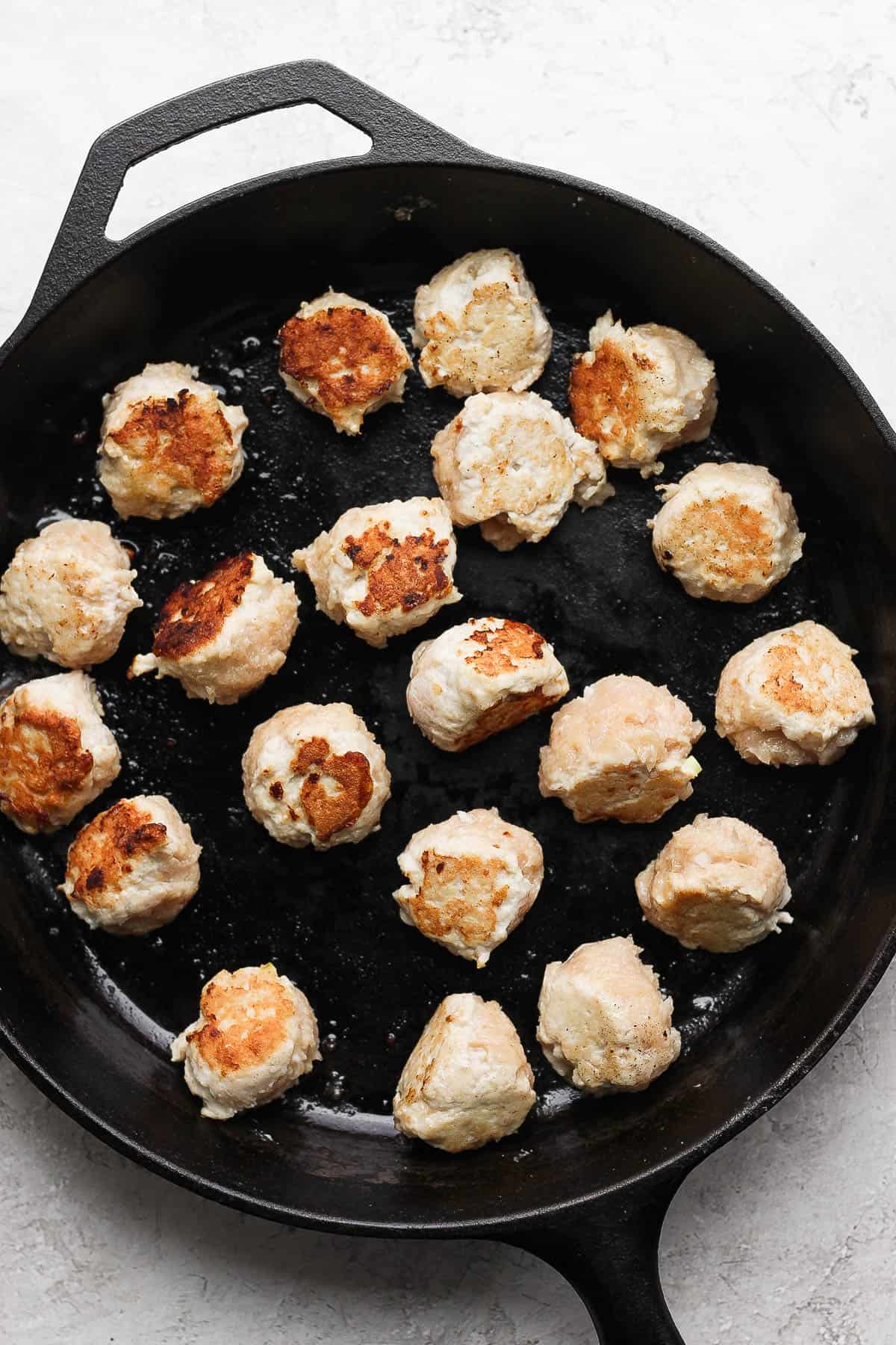 Chicken meatballs searing in a cast iron skillet.
