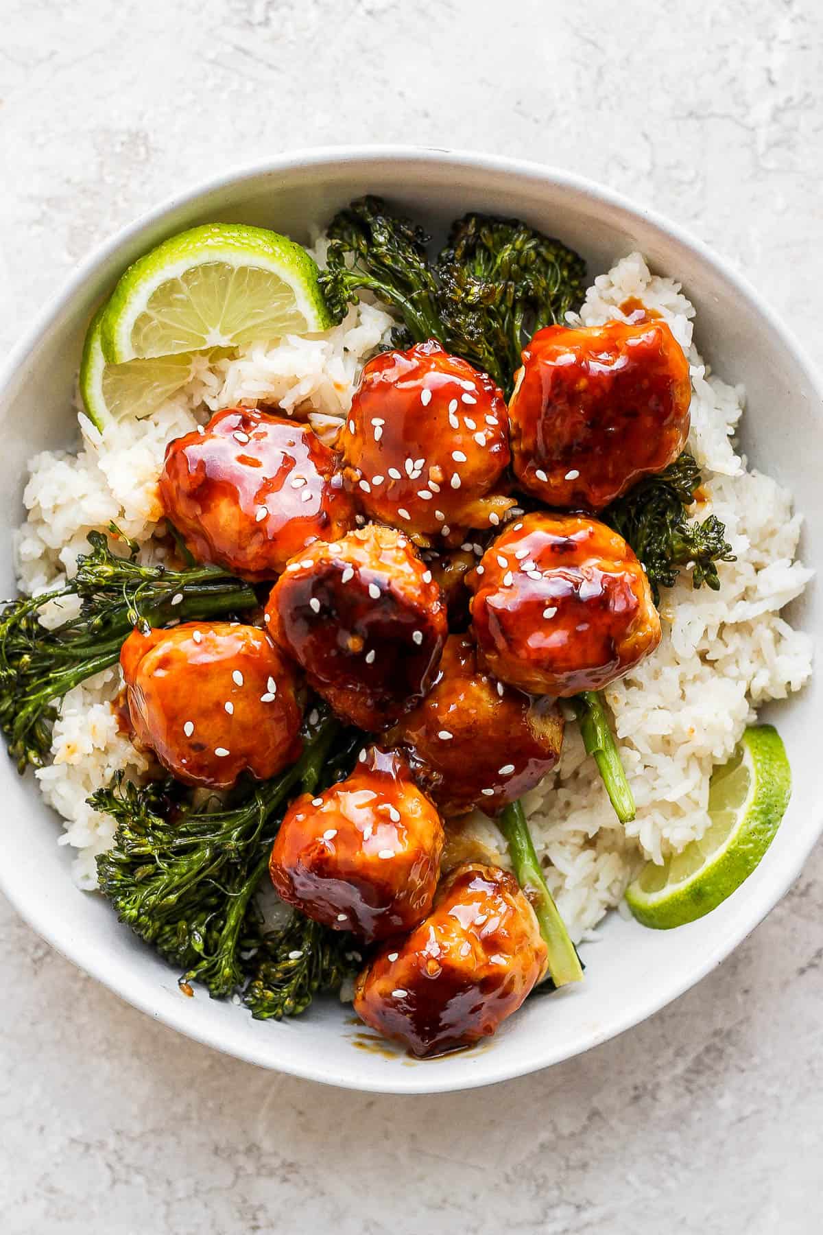 Chicken teriyaki meatballs in a bowl with broccolini and rice.
