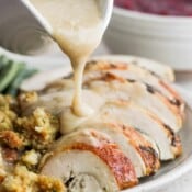 Someone pouring giblet gravy over sliced turkey breast.