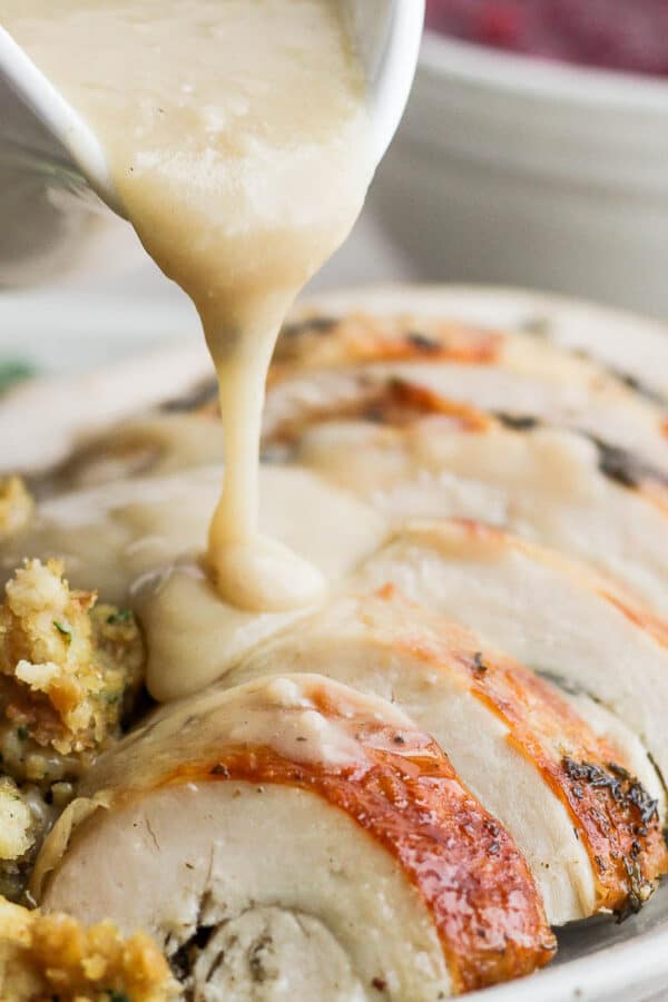 Someone pouring giblet gravy over sliced turkey breast.