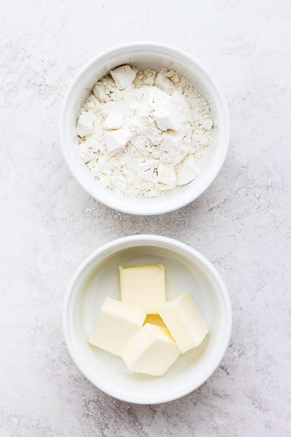 Two white bowls, one with flour and one with butter.