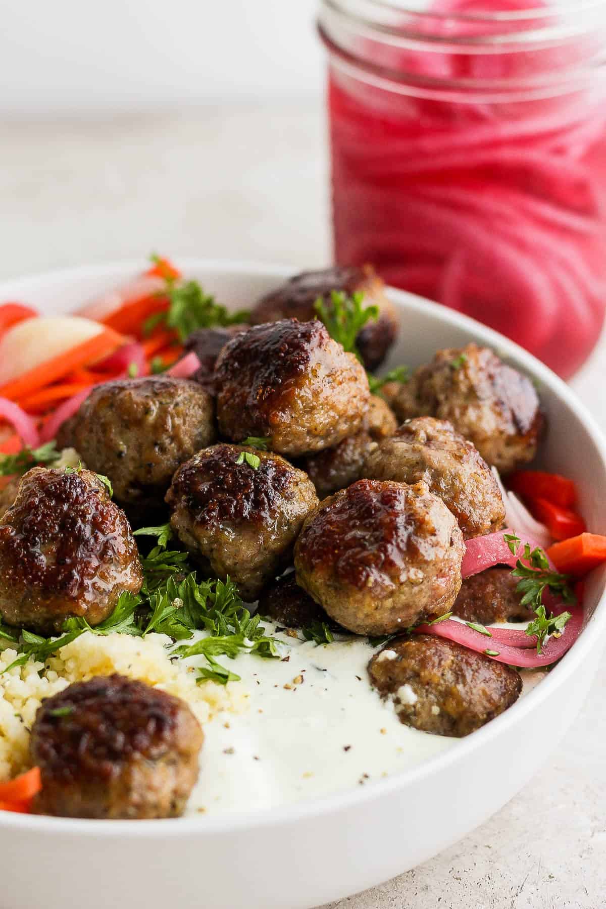 Greek meatballs in a bowl with quinoa, whipped feta, and quick pickled vegetables.