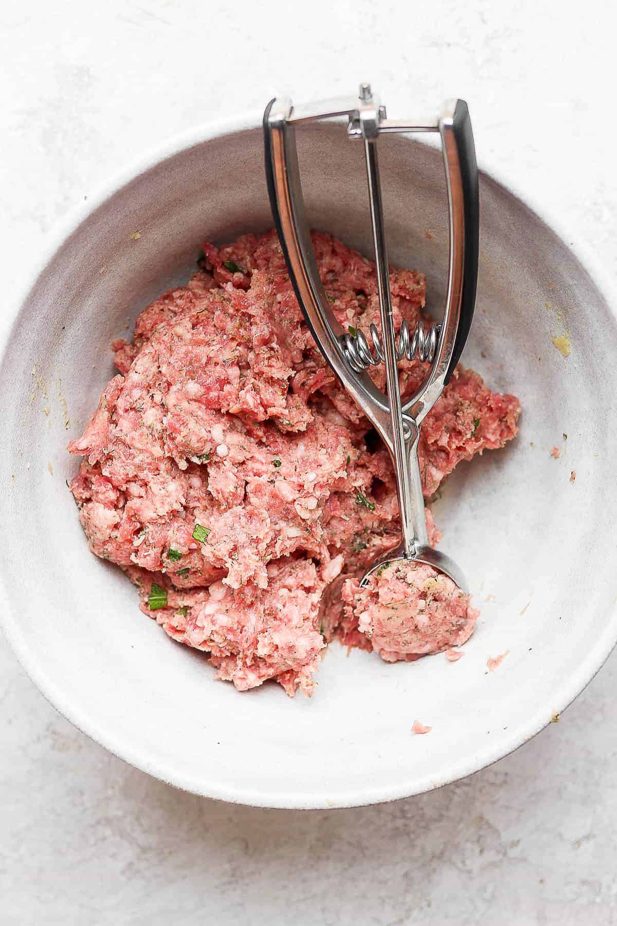 Meatball ingredients mixed together and being scooped with a cookie scoop.