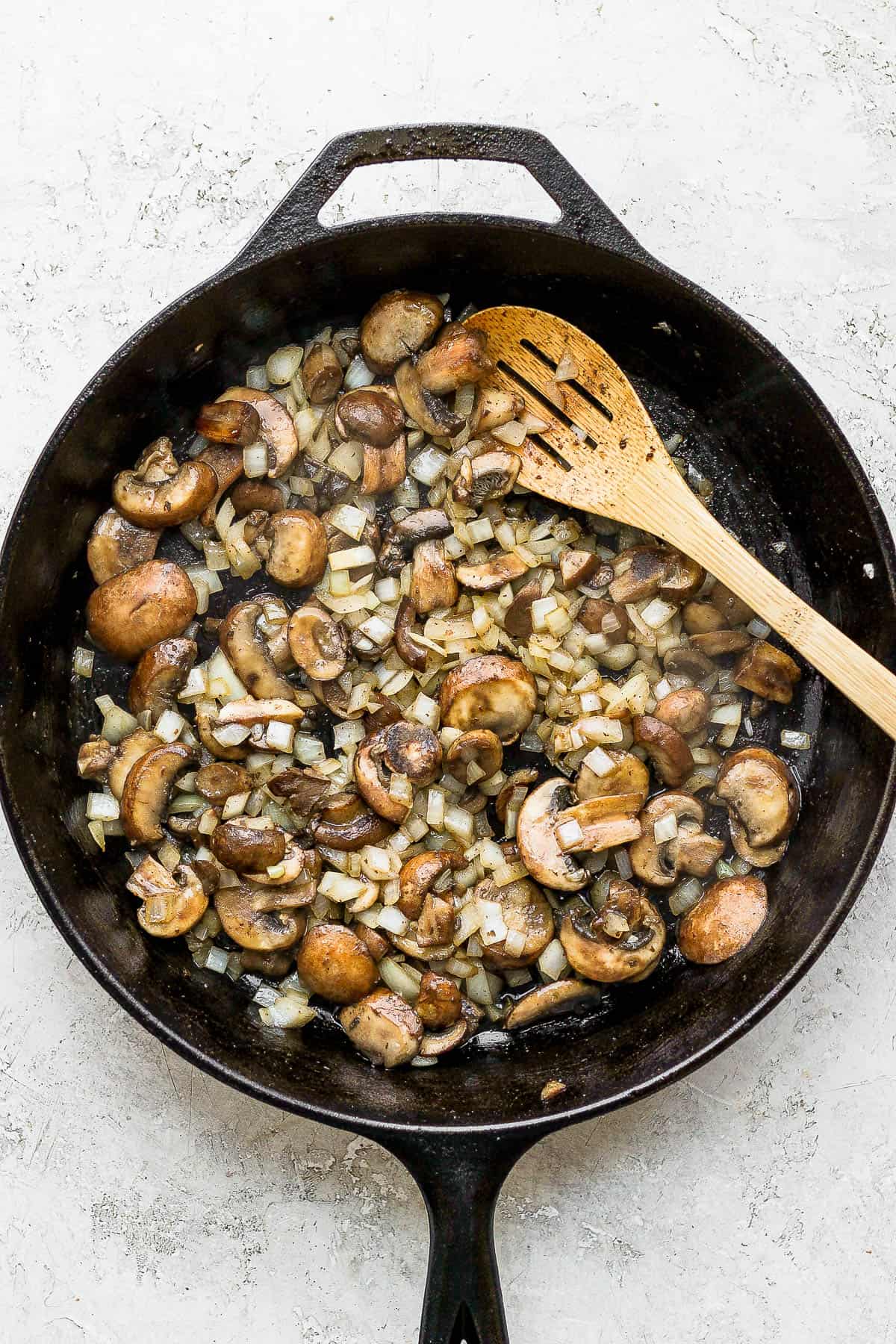 Diced onion, sliced mushrooms, and garlic being cooked in the same cast-iron skillet as the bacon was earlier.